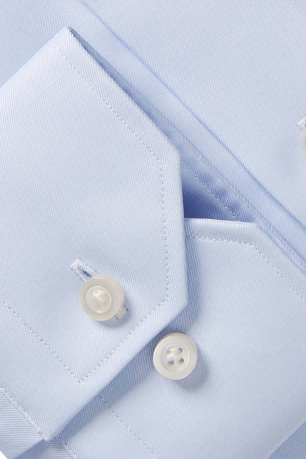 Détail d'une chemise contemporaine bleu avec col classique et boutons blancs, mettant en valeur le tissu texturé.