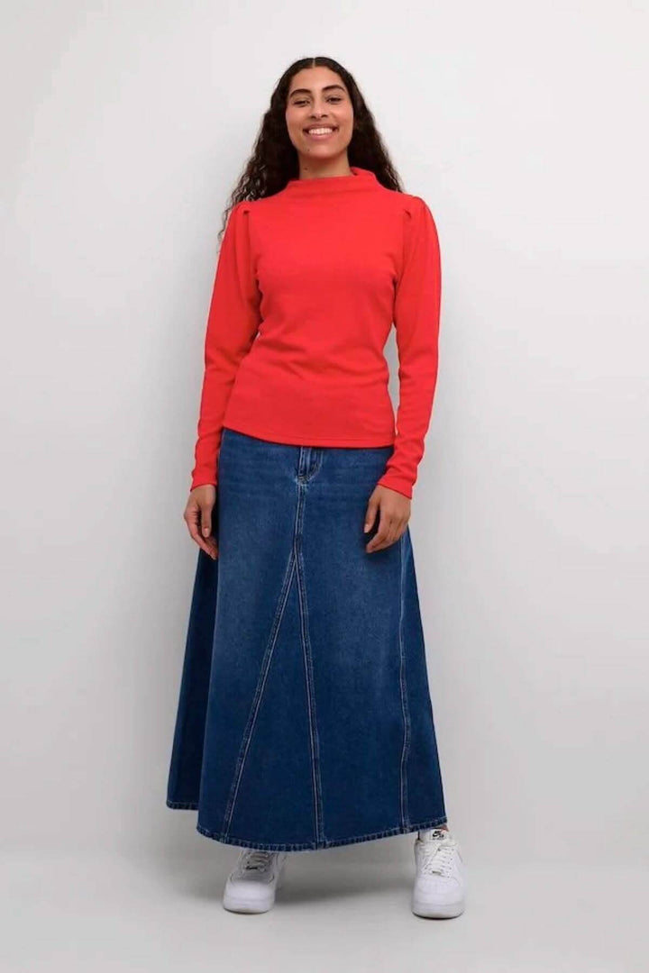 Femme portant un chemisier rouge vif et une jupe en denim, style élégant et décontracté.