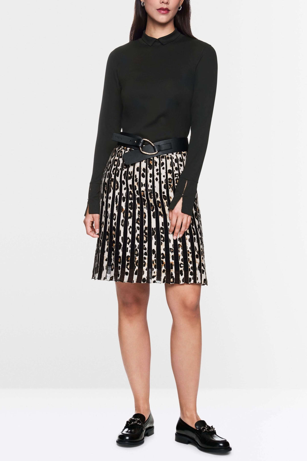 Femme en col roulé ajusté noir et jupe plissée imprimée, look chic avec ceinture large.