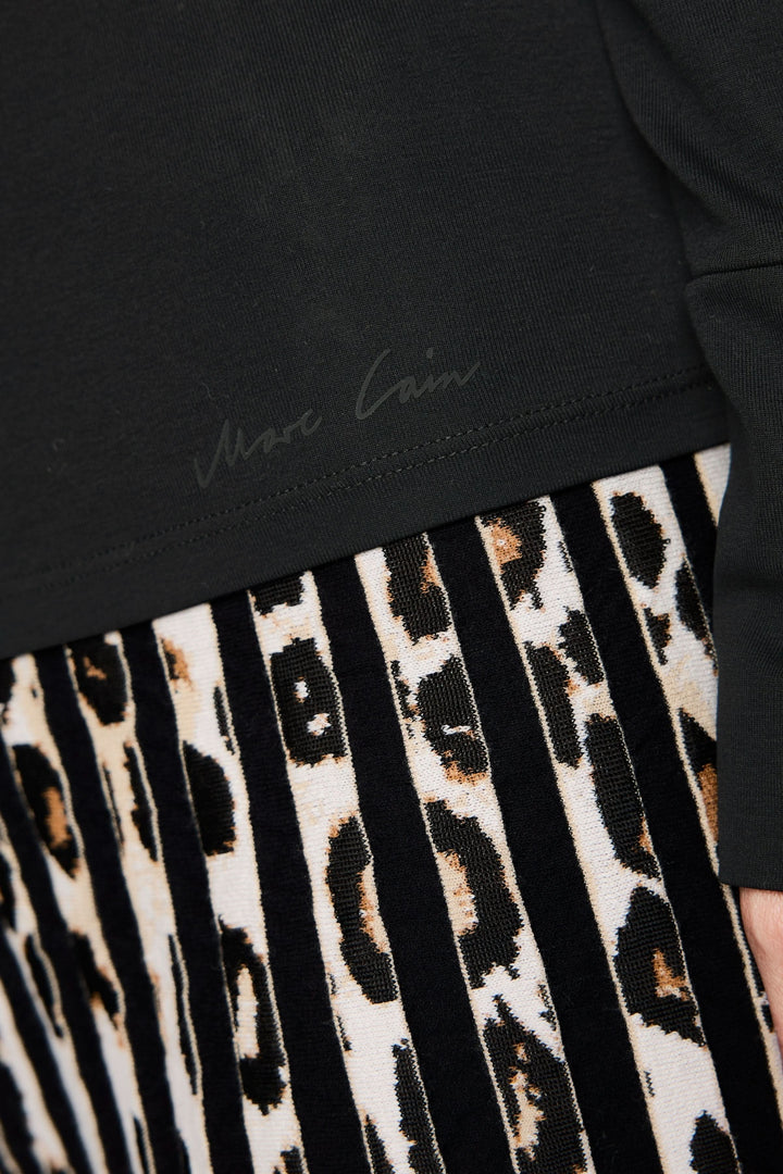 Détail d'un col roulé noir avec signature, associé à une jupe plissée à motifs léopard.