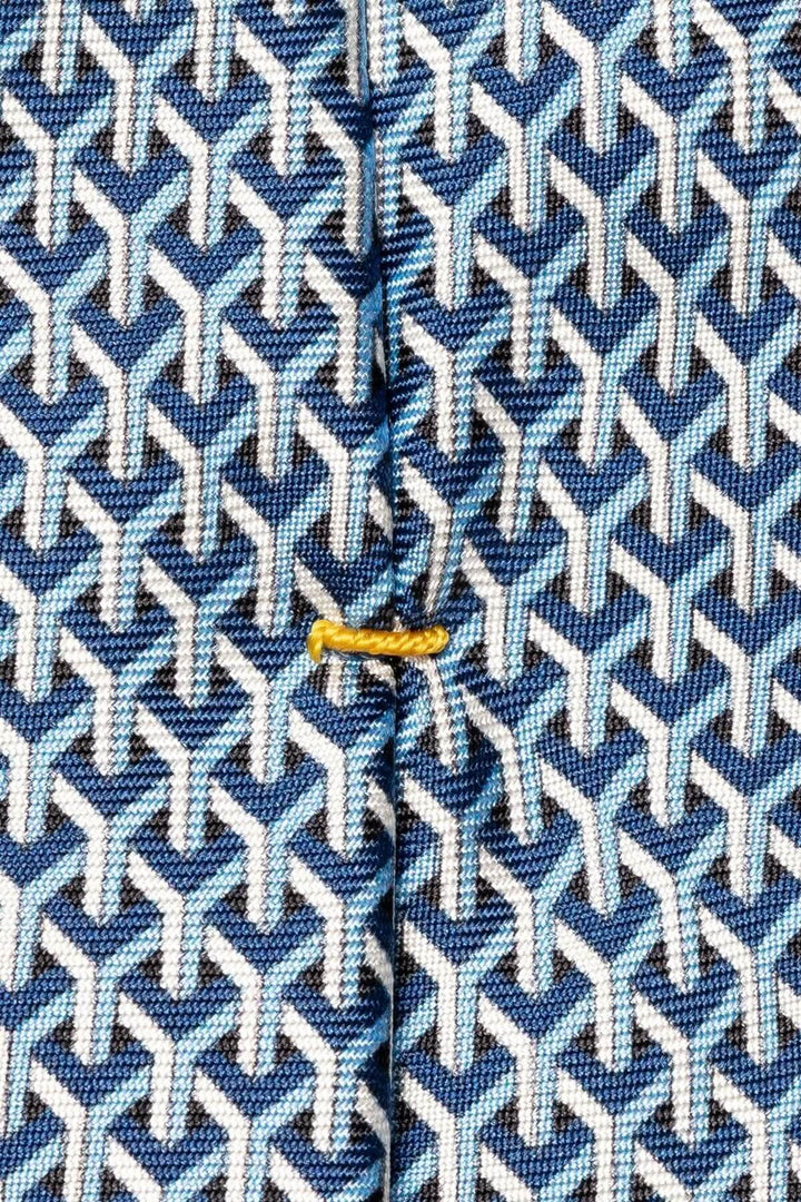 Close-up of a silk tie featuring a structured geometric pattern in navy blue and white with a gold accent.