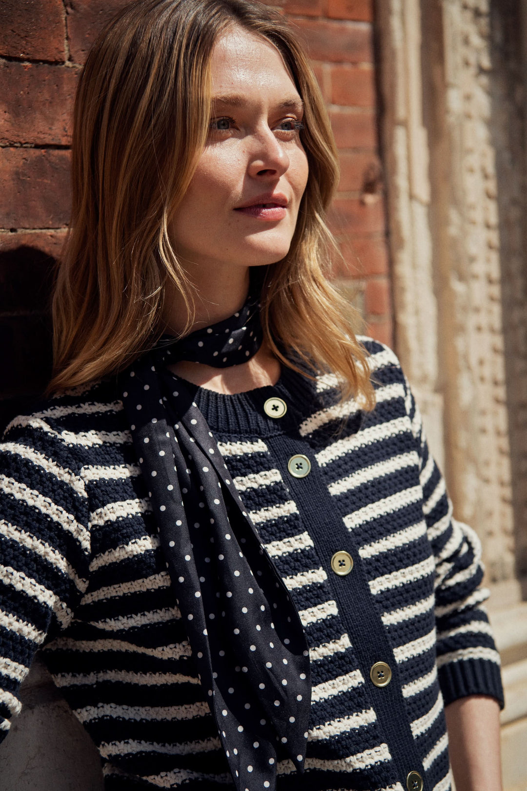 Foulard à pois noir porté avec un cardigan rayé, ajoutant une touche élégante et féminine à la tenue.