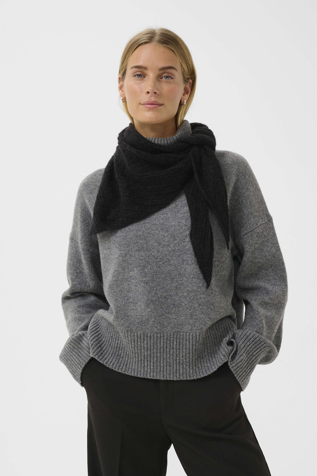 Femme portant un foulard Sizze en tricot léger noir, ajoutant chaleur et style minimaliste à une tenue élégante en gris et noir.