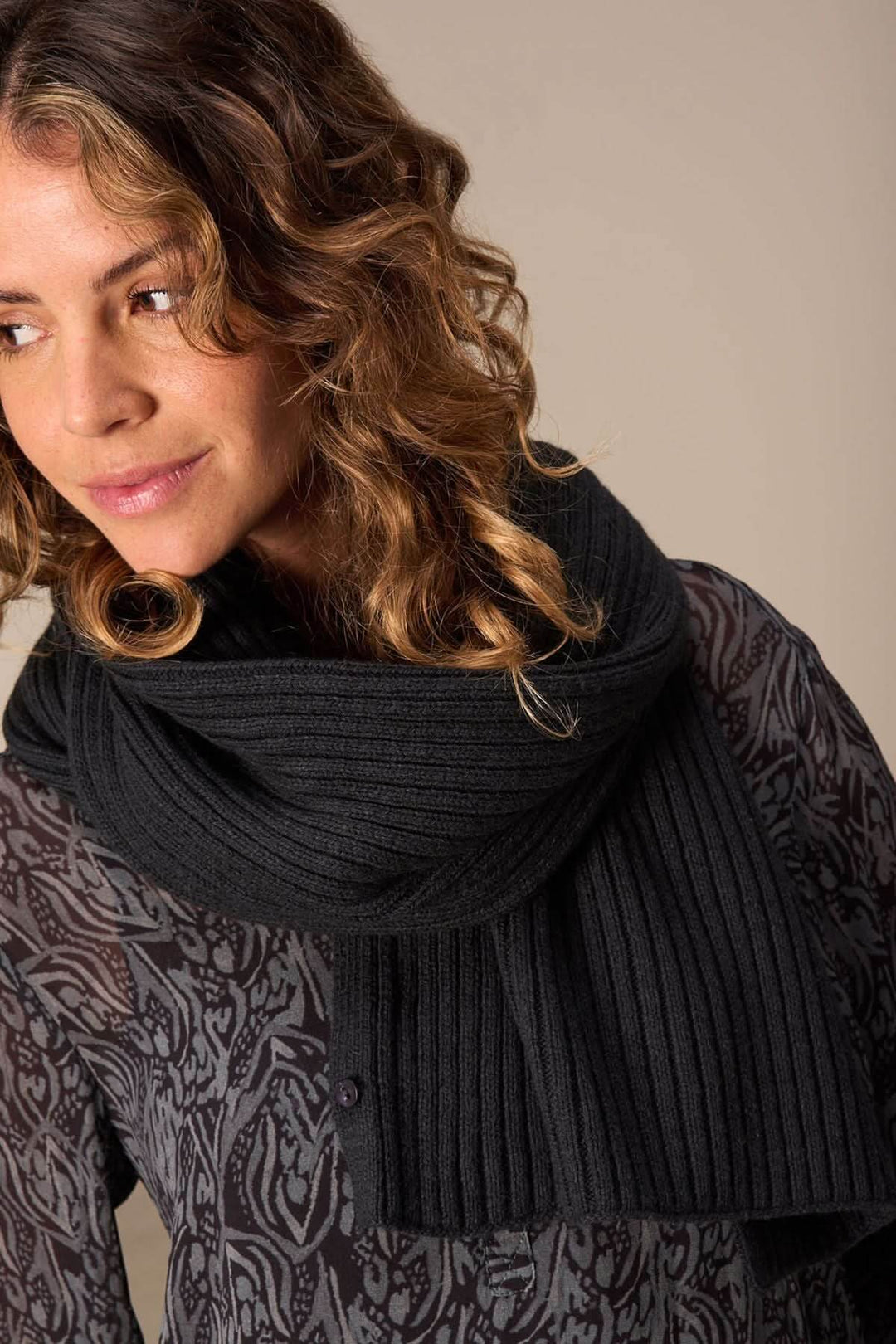Foulard cape en tricot noir, versatile et élégant, porté en écharpe pour un look raffiné.