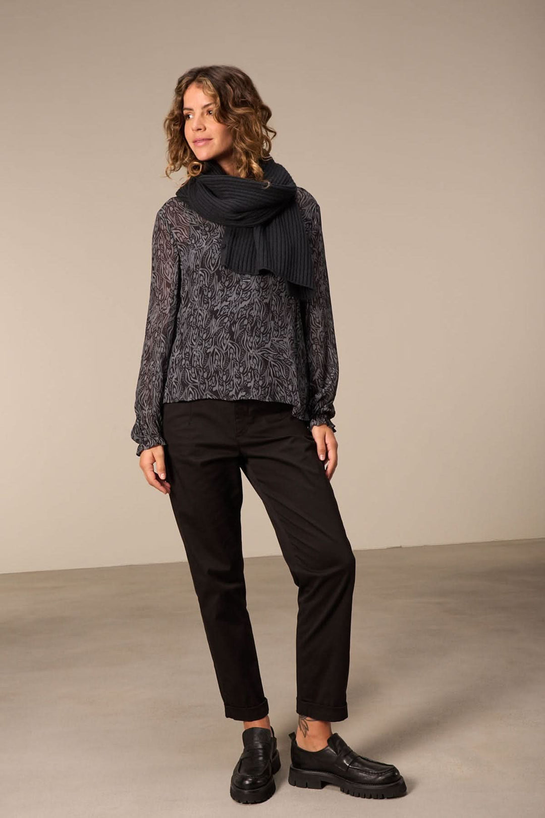 Femme portant un foulard en tricot noir avec un pull et un pantalon noir, dans un cadre élégant.