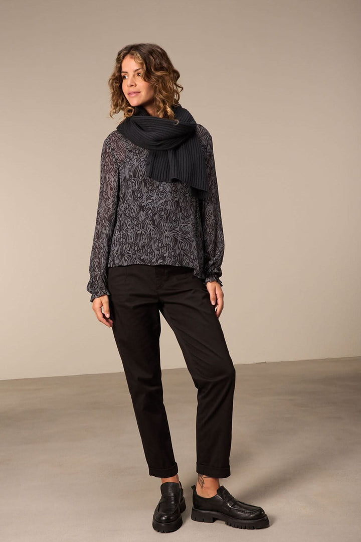 Femme portant un foulard en tricot noir avec un pull et un pantalon noir, dans un cadre élégant.