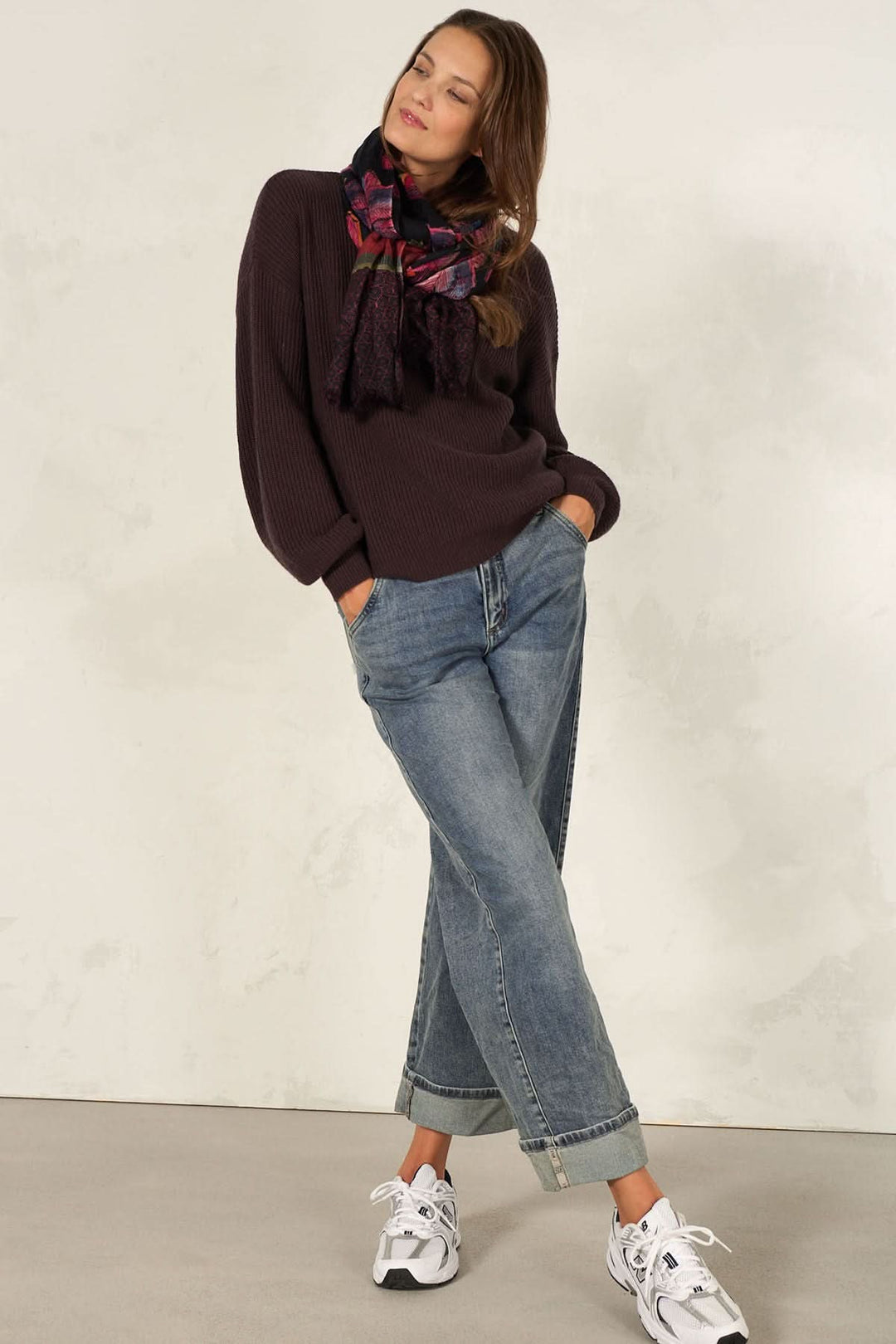 Femme portant un foulard décoratif, pull confortable et jeans, style élégant avec des baskets blanches.