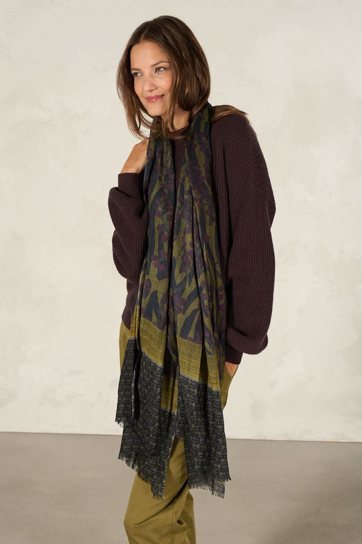 Foulard décoratif avec imprimés artistiques porté sur un pull, ajoutant élégance à une tenue casual.