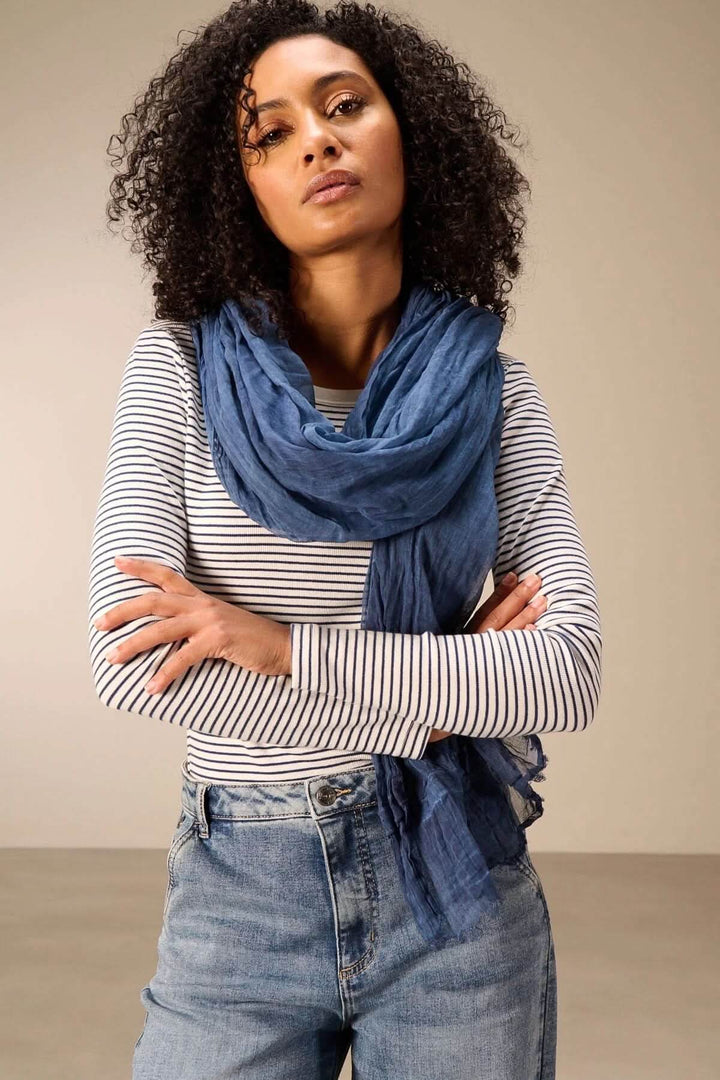 Femme portant un foulard en coton bleu, léger et fluide, avec une tenue décontractée. Accessoire parfait pour un style élégant et naturel.