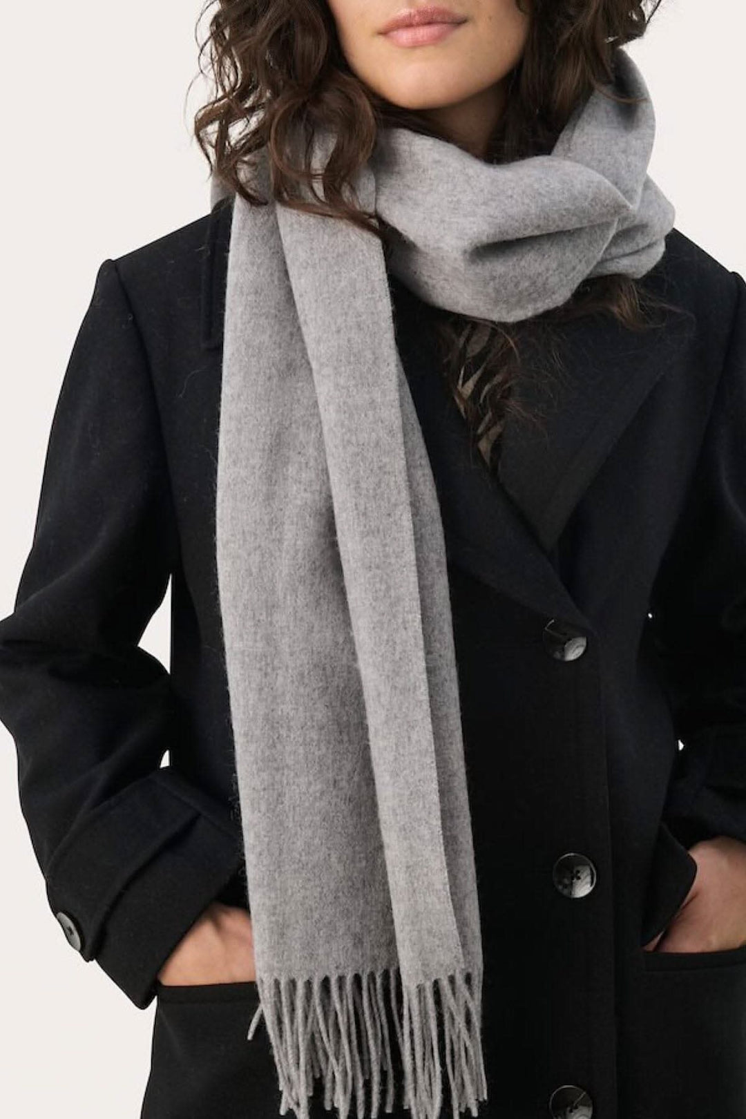 Foulard en laine Kitha gris porté avec un manteau noir, ajoutant chaleur et style aux tenues d'hiver.