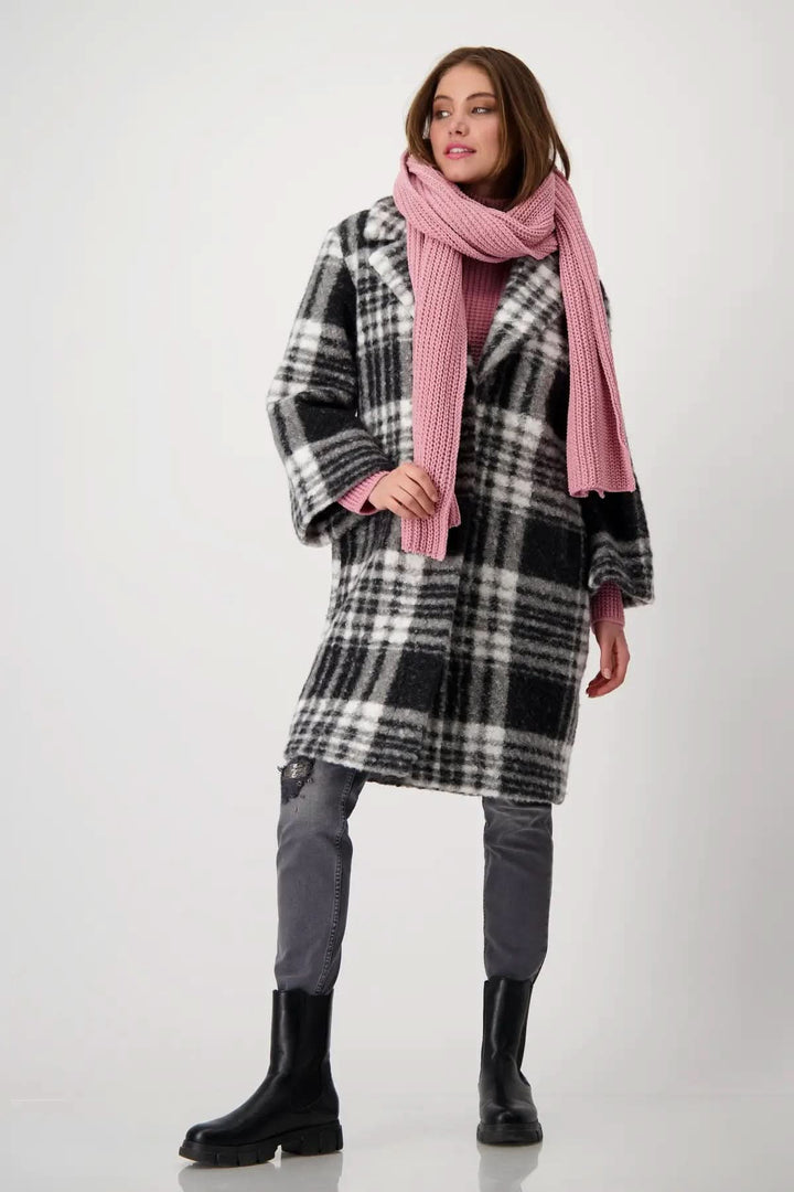 Femme portant un manteau à carreaux noir et blanc avec une écharpe en tricot rose, style moderne et confortable.
