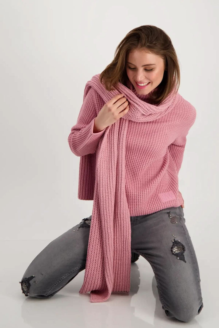 Foulard en tricot rose porté par une femme souriante, ajoutant confort et style à sa tenue décontractée.