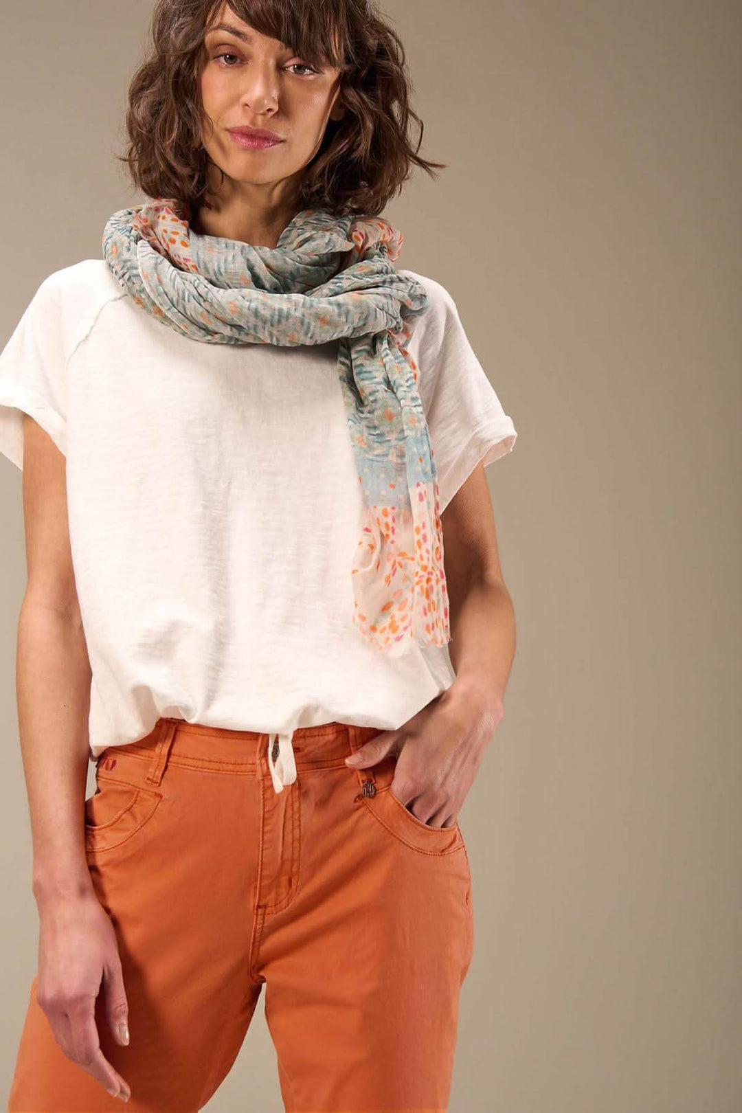 Foulard imprimé en coton bio porté avec un t-shirt blanc et un pantalon orange, ajoutant une touche sophistiquée.