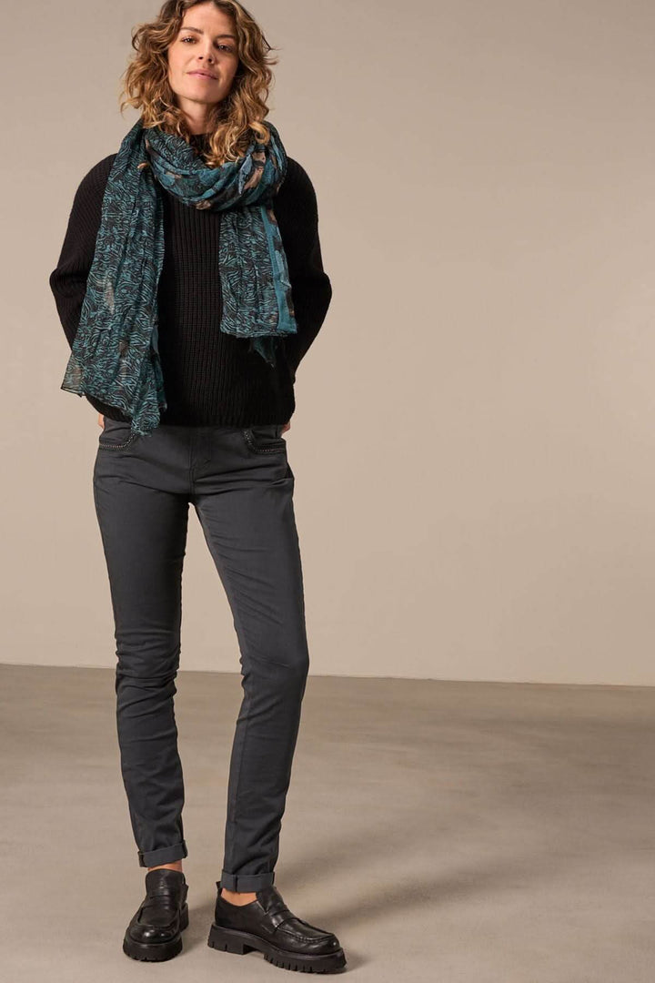 Femme portant un foulard paréo élégant avec un pull noir et un pantalon gris, look chic et décontracté.