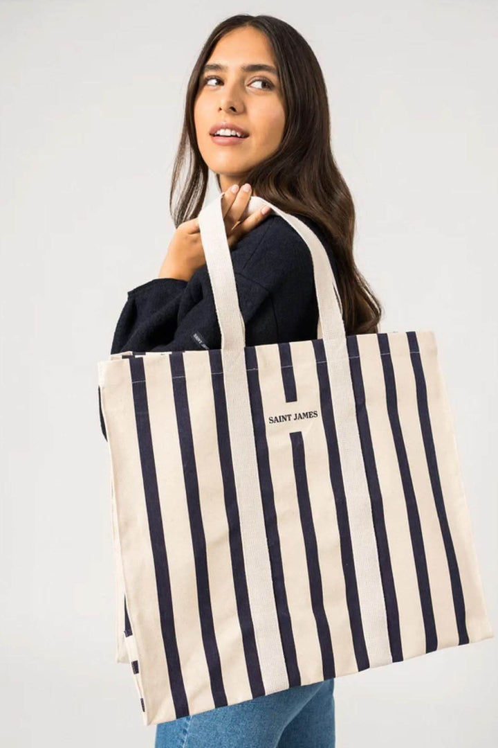 Femme souriante portant un cabas en coton rayé SAINT JAMES, parfait pour la plage.