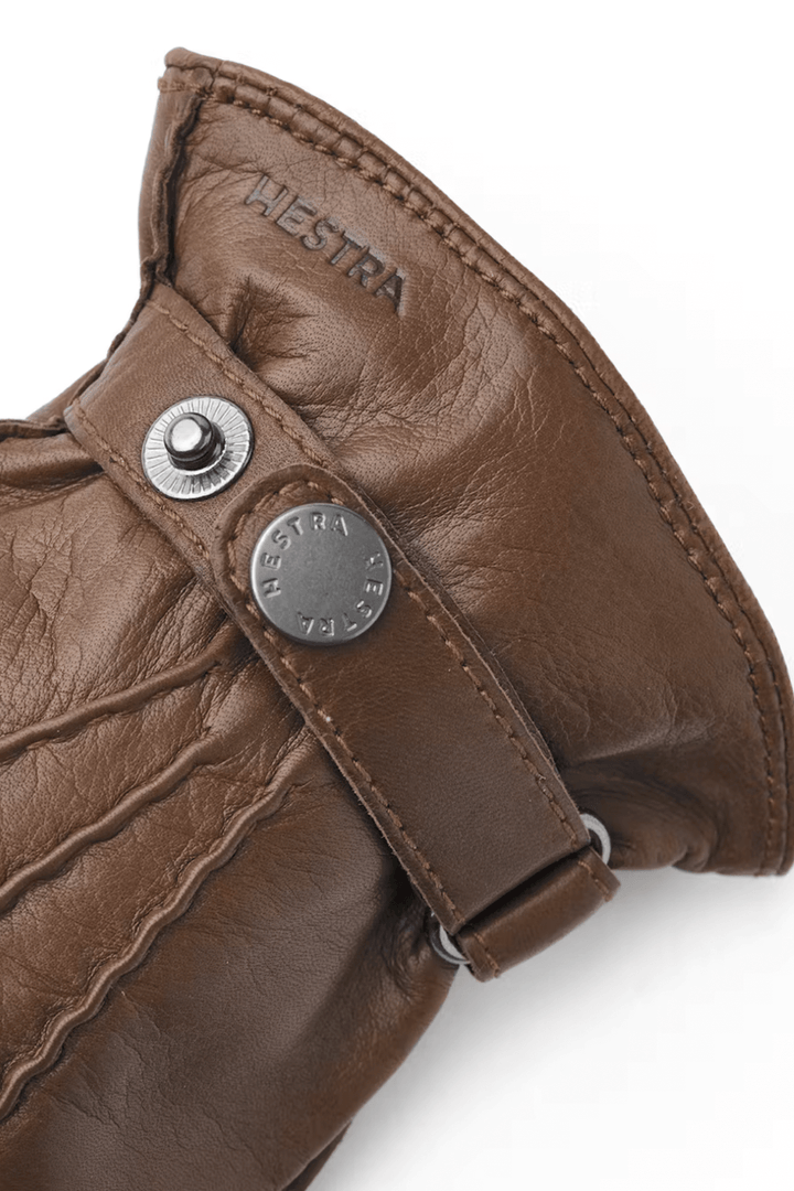Détails des gants en cuir Hestra avec bride et bouton pression, couleur marron, cuir souple et élégant.