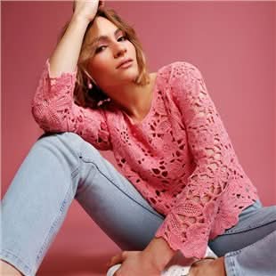 Femme portant un haut en tricot ajouré rose avec un motif floral, assise contre un fond rose.