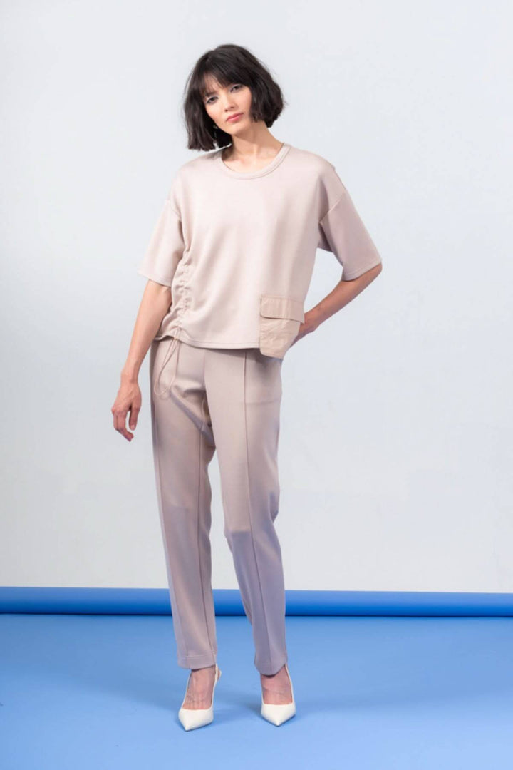 Haut à manches courtes beige avec encolure ronde et poche, porté avec un pantalon assorti.