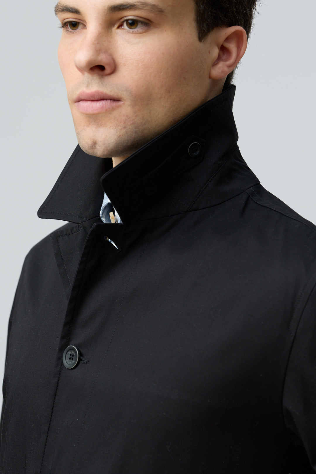 Homme portant un impermeable en gabardine de coton noir avec col chemise et coupe droite élégante.
