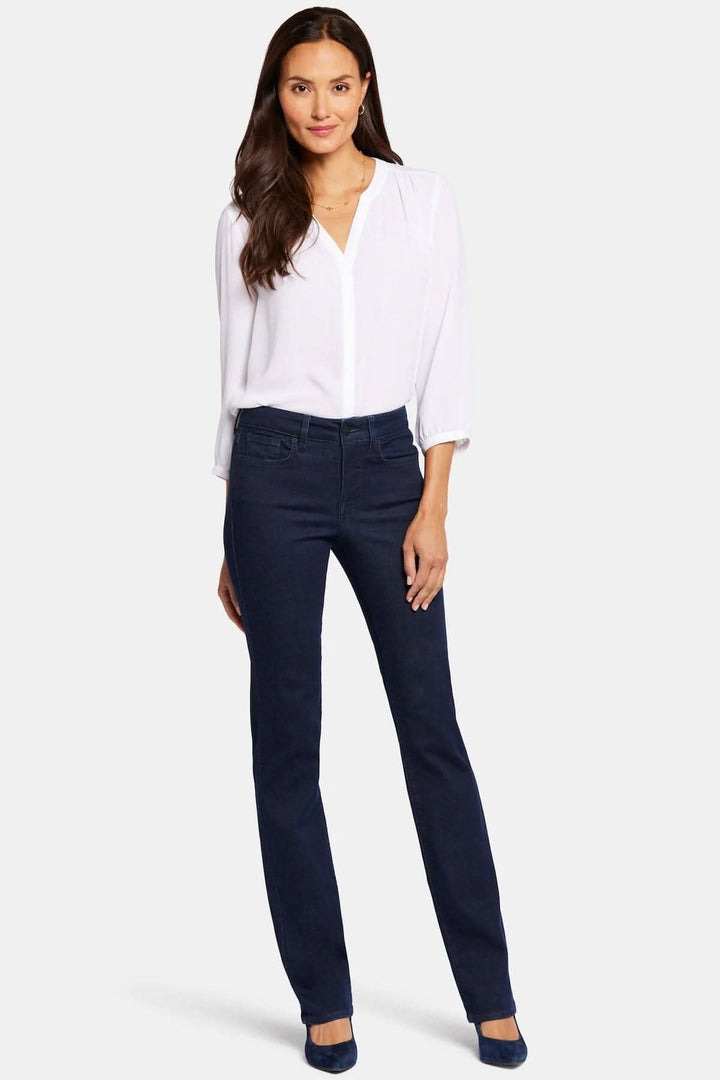 Femme portant un jean droit Marilyn, coupe flatteuse, style classique à cinq poches, avec blouse blanche.