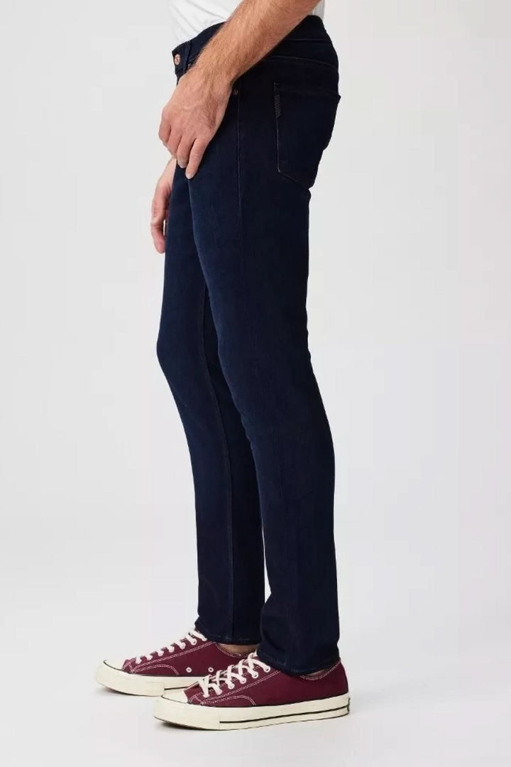 Homme portant le jean slim Lennox de Paige en délavage indigo foncé, associé à des chaussures rouges.