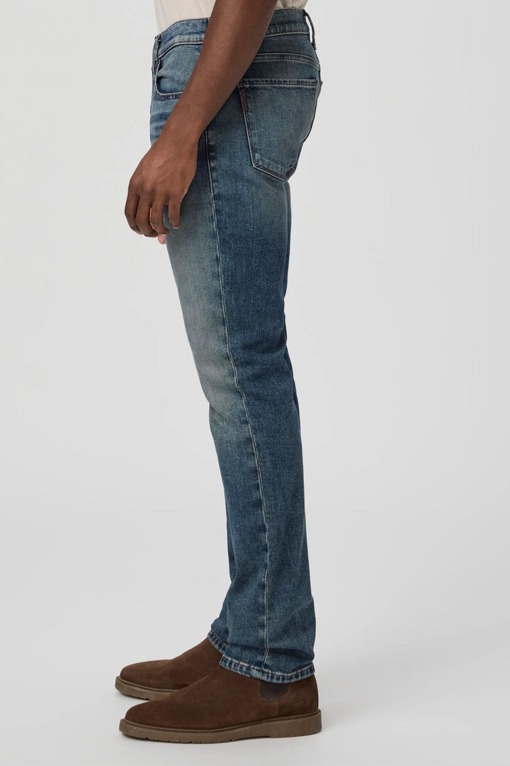 Jean ajusté slim fit avec délavé vintage, offrant confort et liberté de mouvement, porté avec des chaussures marron.