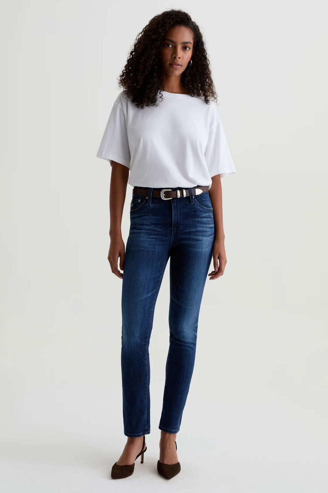 Jean ajusté à taille mi-haute porté avec un t-shirt blanc et des talons marrons, offrant un look décontracté-chic et polyvalent.