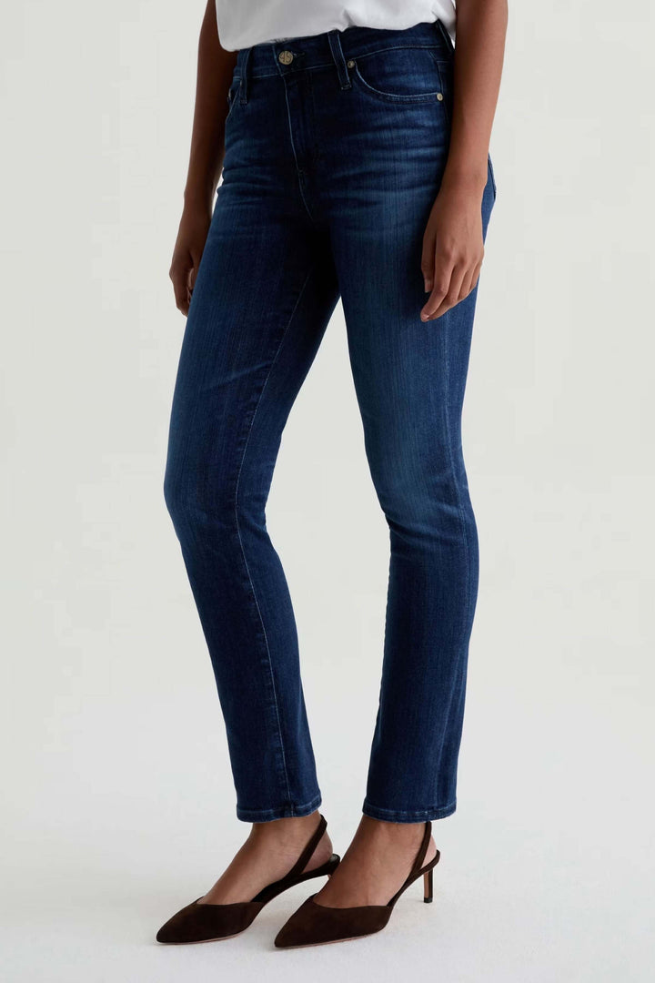 Jean ajusté à taille mi-haute en denim extensible bleu, silhouette féminine avec talons, look décontracté-chic.
