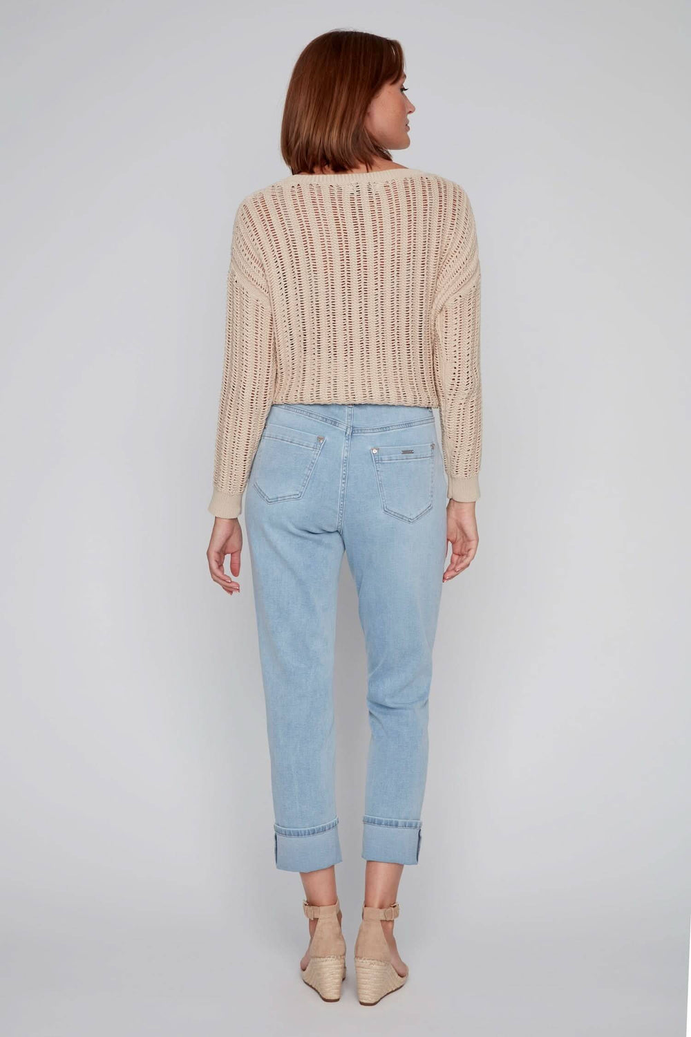 Femme de dos portant un pull beige et un jean décontracté bleu clair avec revers, look estival.