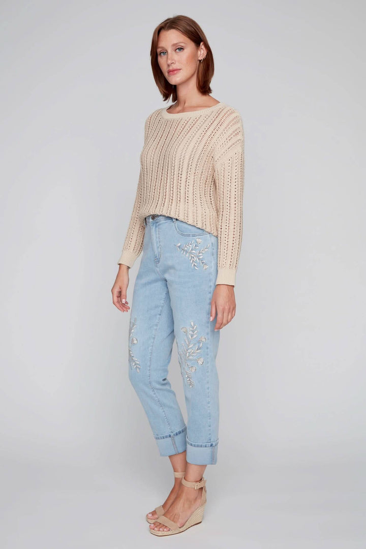 Femme portant un jean à broderies florales et un pull beige, style estival décontracté.