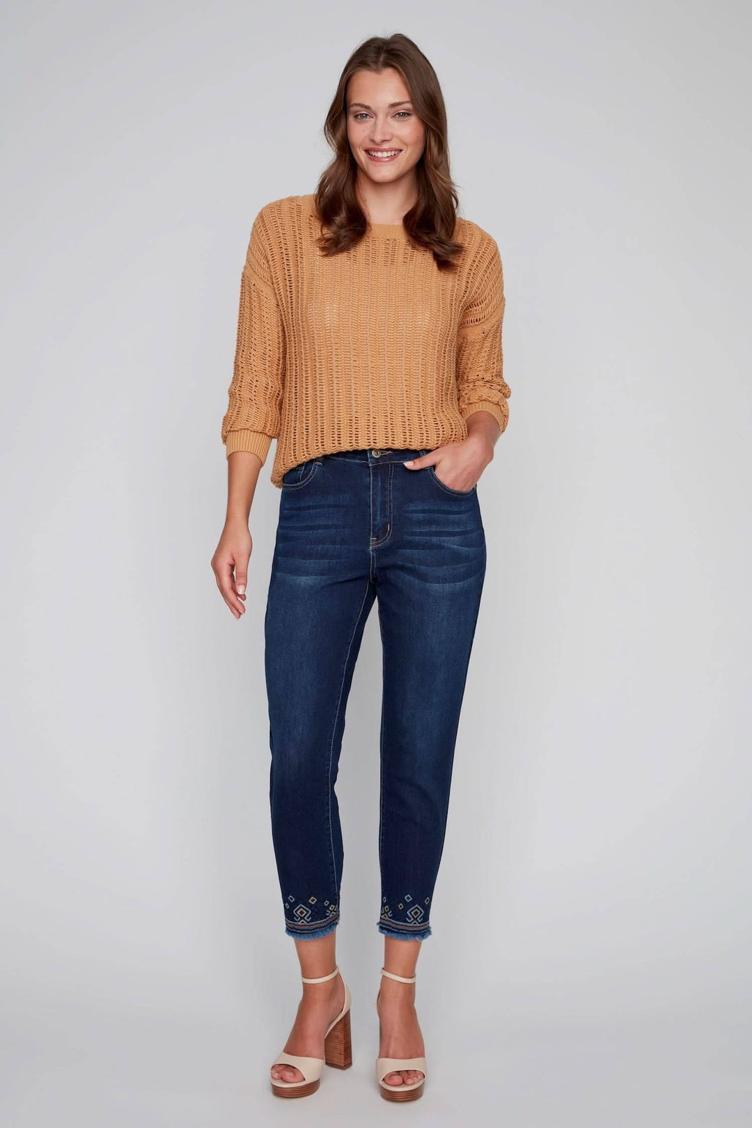 Jean avec broderies géométriques colorées, style chic-décontracté porté avec un pull en maille beige.