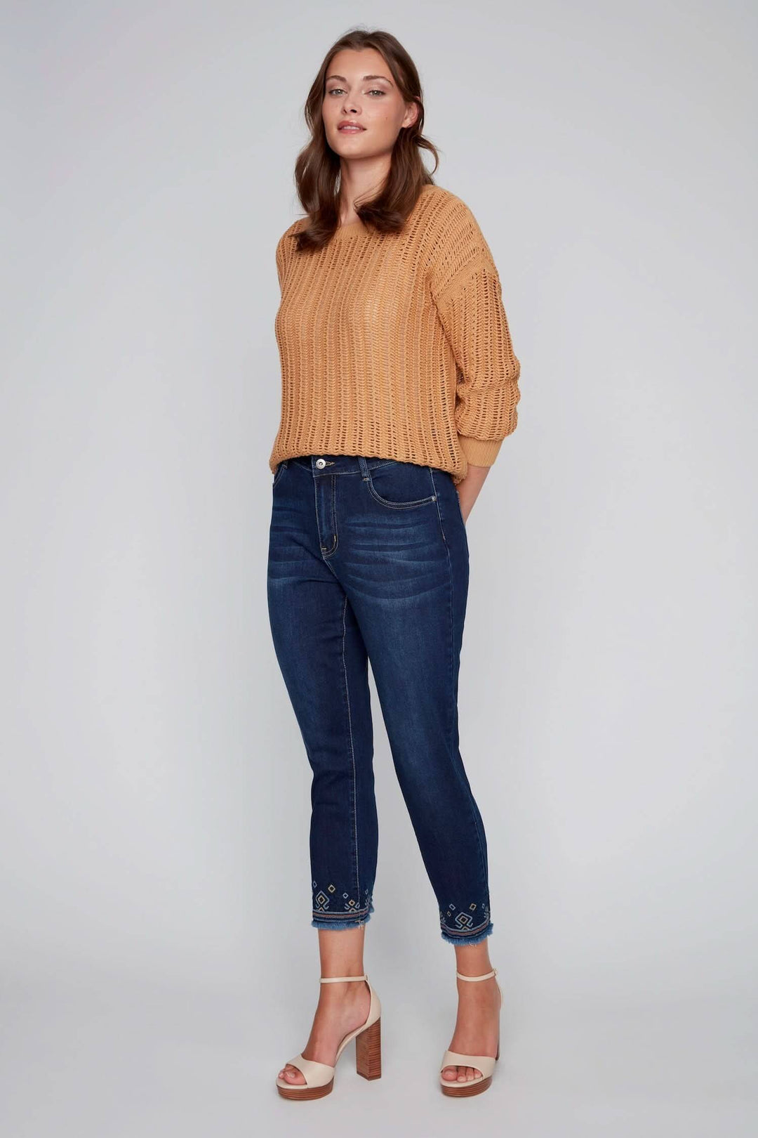 Jean à jambe droite avec broderies géométriques au bas, porté avec un pull beige, pour un look chic-décontracté.