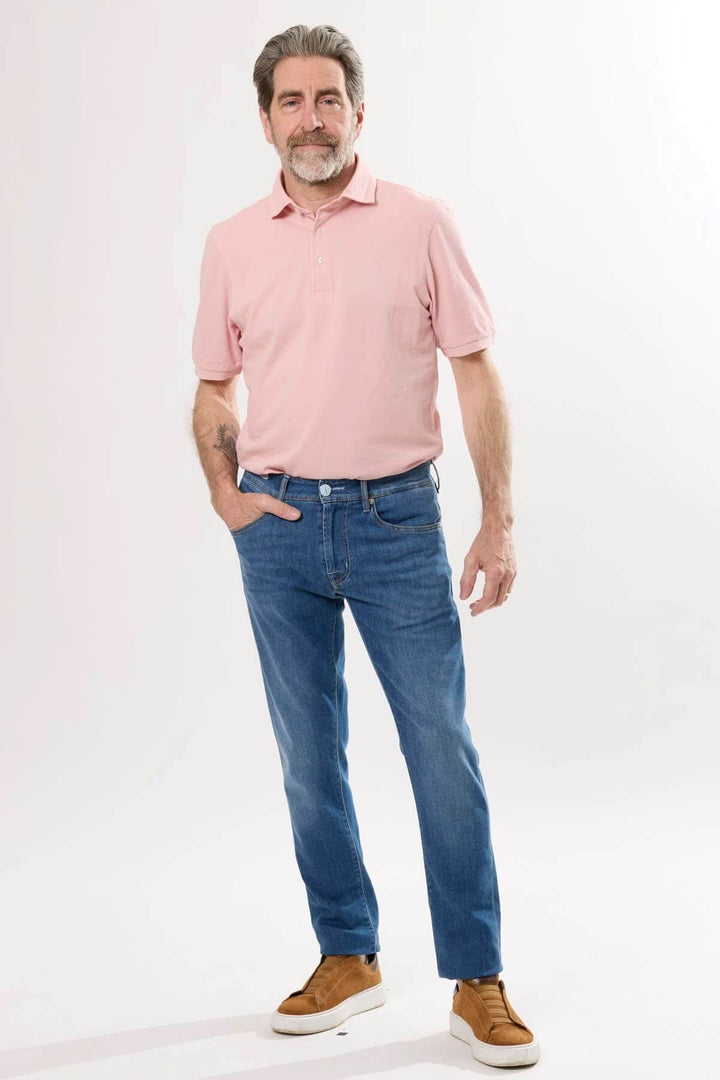 Homme portant un polo rose et un jean coupe droite délavé pour un look décontracté et soigné.
