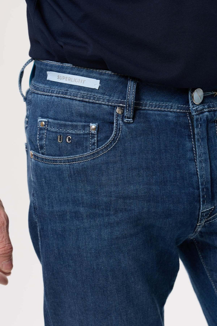 Jean coupe droite en denim bleu avec toile extensible, finition légèrement délavée et logo sur la poche arrière.