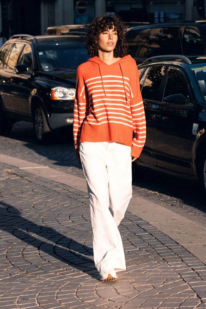 Person walking in Jean jambe large and striped orange hoodie on cobblestone street.