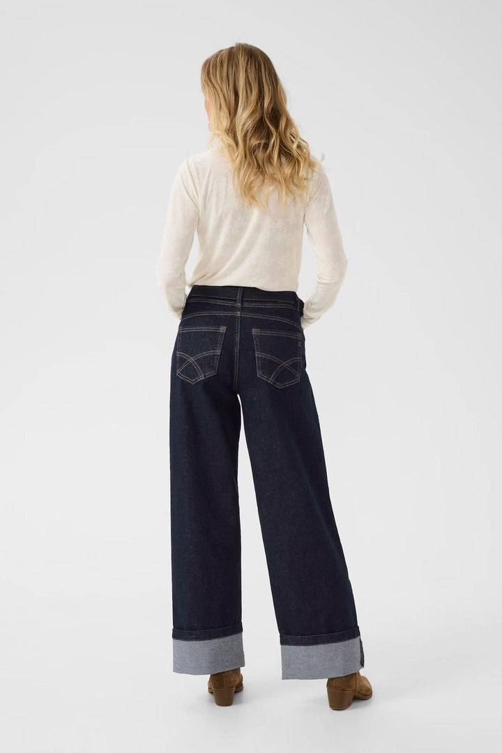 Femme portant un jean à jambe large avec revers, vu de dos, associé à un haut beige.