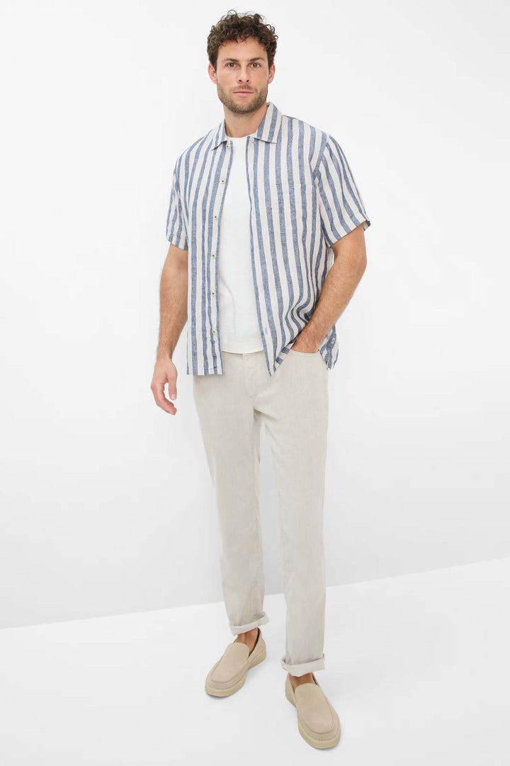 Homme portant une chemise à rayures bleu et blanc avec un t-shirt blanc et un pantalon léger beige, style décontracté.