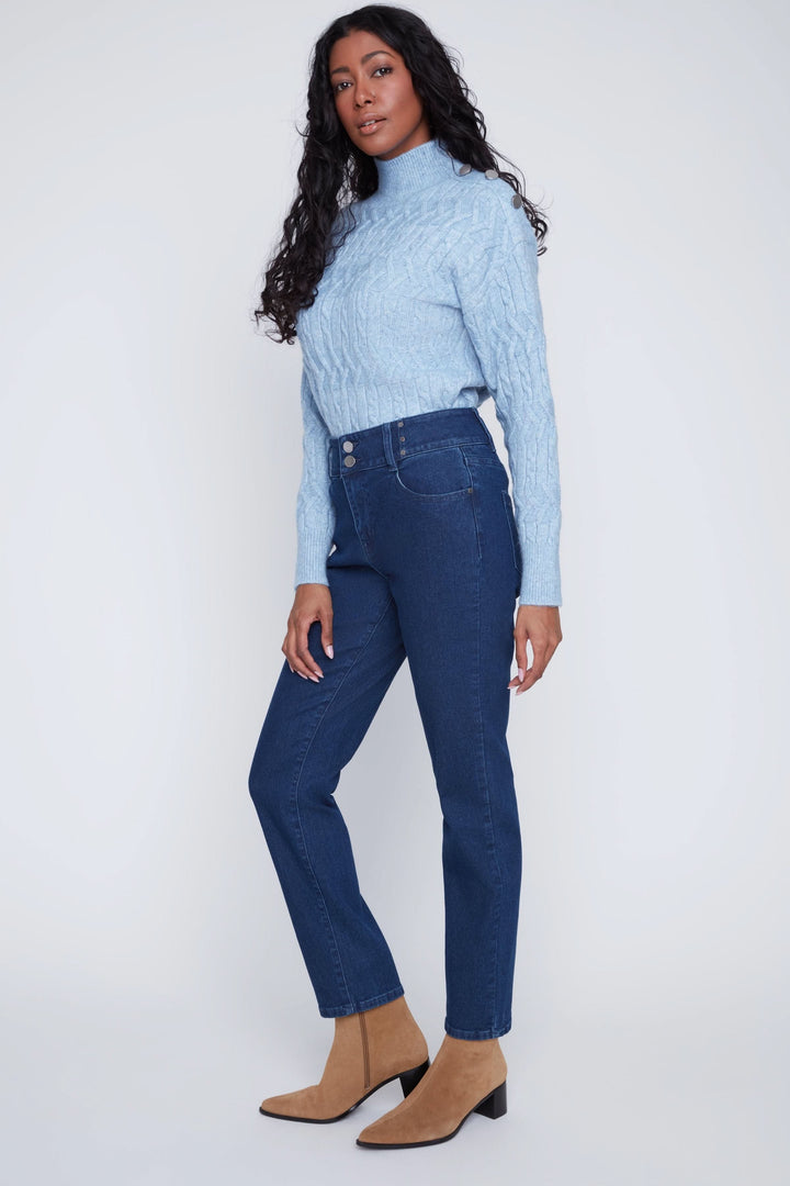 Jean taille haute avec coupe droite, porté avec un chandail bleu et bottines beiges, look moderne et élégant.