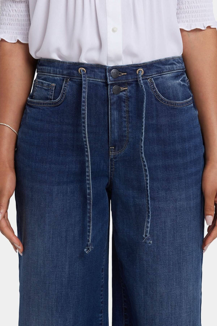 Jean Cindi à jambe large avec taille haute et cordon ajustable, parfait pour un look décontracté et moderne.