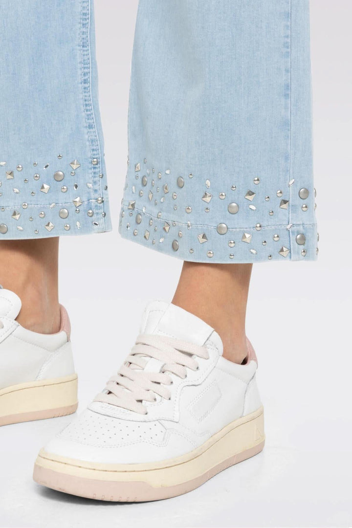 Détail de jeans culotte en denim léger avec studs brillants, porté avec des baskets blanches pour un look moderne.