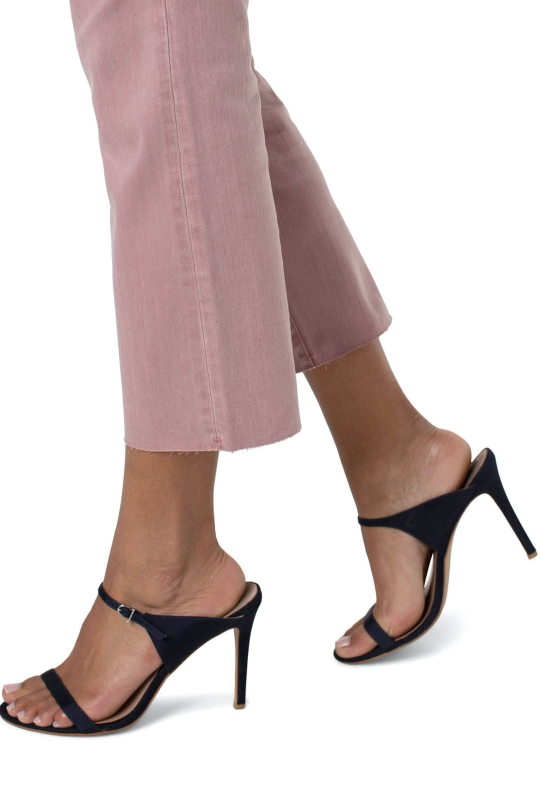 Femme portant des sandales noires à talons avec un jeans rose, style chic et décontracté.