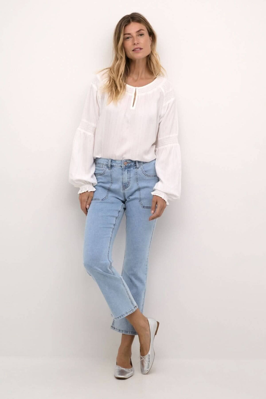 Femme portant un jean bleu clair à coupe droite avec une blouse blanche et des chaussures argentées.