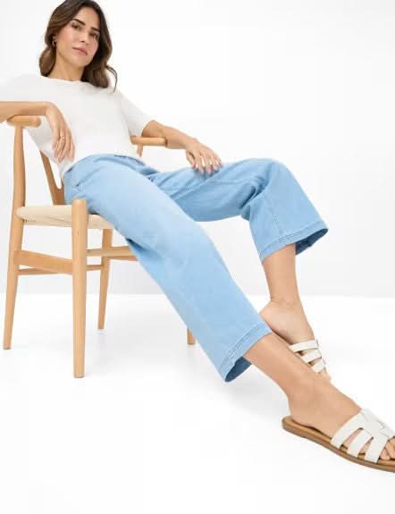 Femme assise sur une chaise, portant le jeans MAINE S bleu, avec un haut blanc et des sandales.