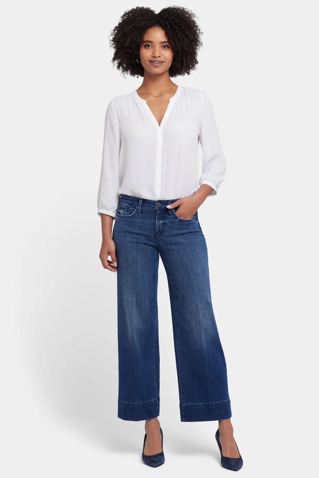 Femme portant les jeans Teresa de NYDJ avec une blouse blanche, affichant un look chic et contemporain.