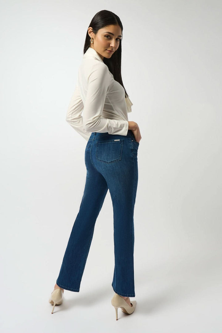 Femme portant des Jeans bleu classique à coupe droite et légèrement évasée, avec talons, contre un fond blanc.