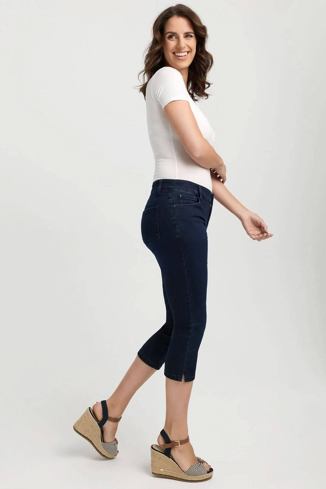 Femme souriante portant un jean capri ajusté, associé à un t-shirt blanc et des sandales, idéal pour l'été.