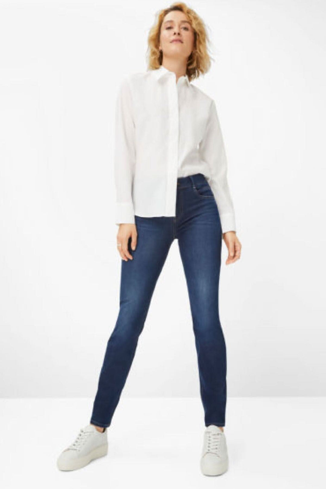 Femme en jeans skinny modernes Shakira, style classique, avec chemise blanche et baskets blanches.