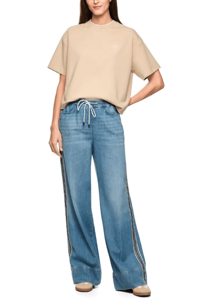 Jeans large à bandes contrastantes avec taille élastique et cordon, style moderne et sportif, porté avec un t-shirt beige décontracté.