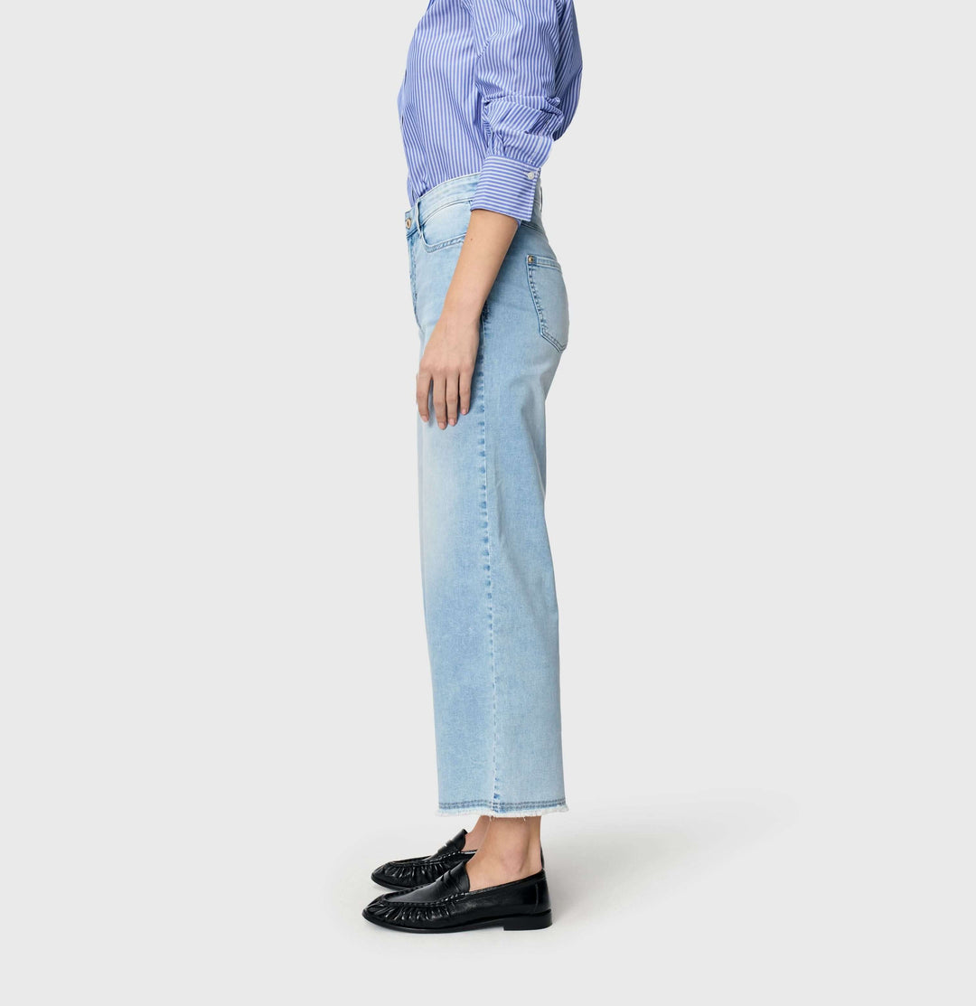 Jeans léger Dream wide cropped, coupe ample, portés avec une chemise bleue et des mocassins noirs sur fond gris.