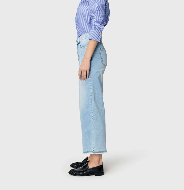 Jeans léger Dream wide cropped, coupe ample, portés avec une chemise bleue et des mocassins noirs sur fond gris.